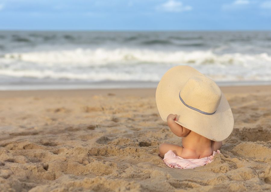 naked baby on virginia beach oceanfront holding a beach hat on head, ocean waves crashing in on the shoreline