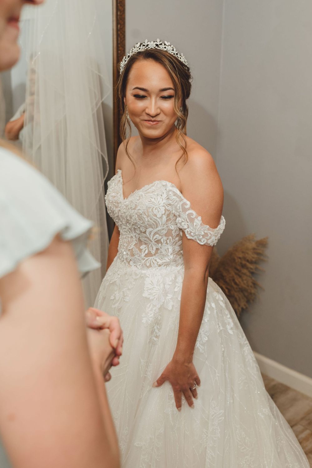 A bride in an elegant off-shoulder lace wedding gown with a flowing skirt poses during her getting ready session.