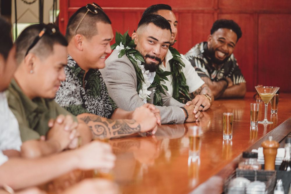Wedding party enjoying drinks and conversation at a rustic wooden table with red wall backdrop.