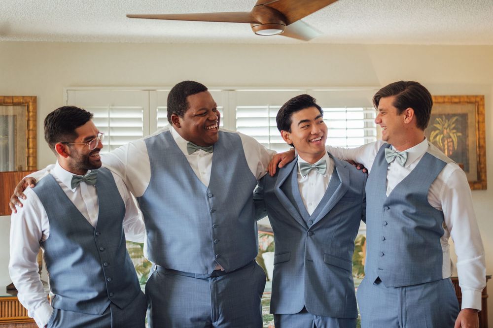 Groomsmen lined up wearing matching light gray vests and white dress shirts for wedding photos.