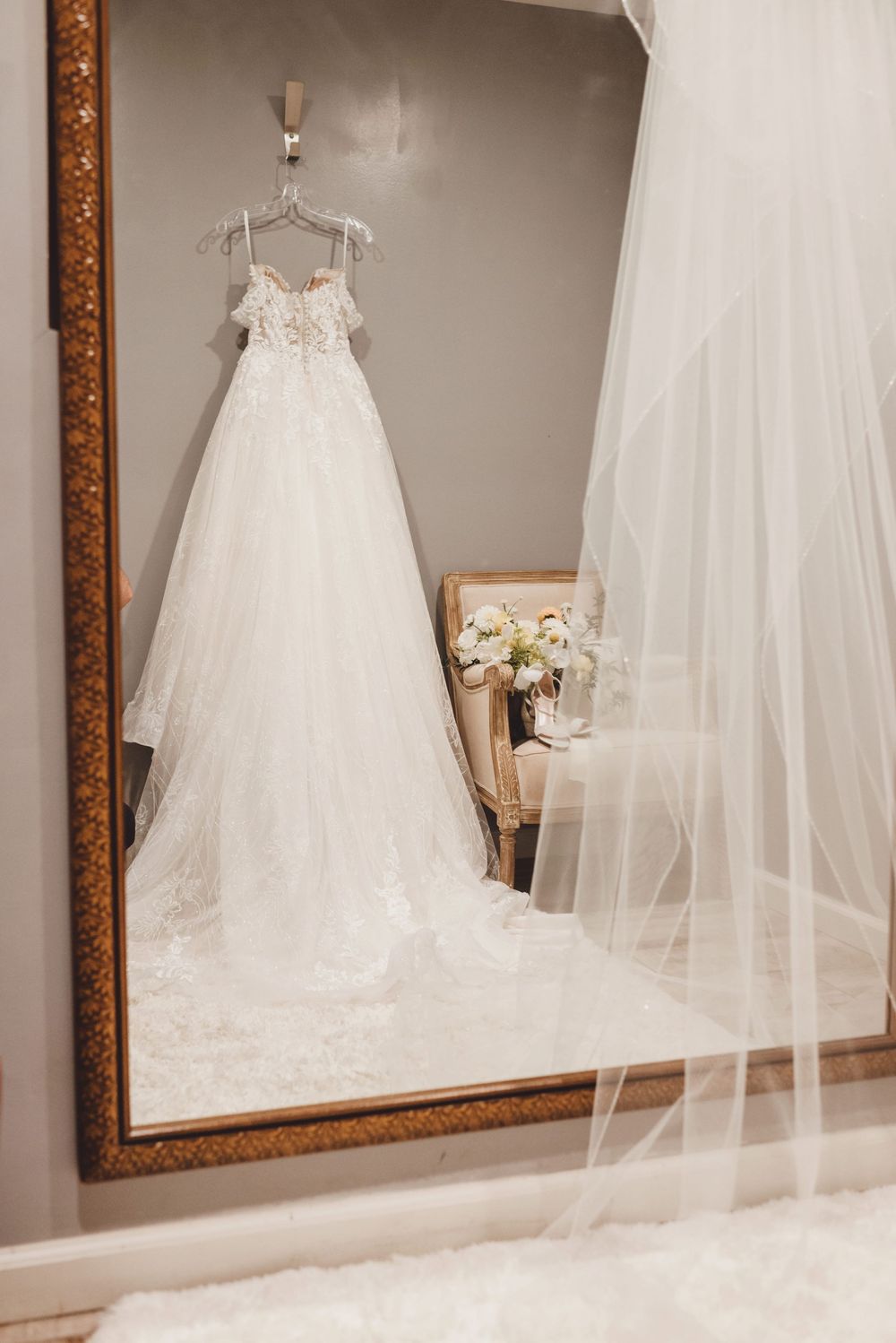 Elegant white wedding dresses and veils displayed in a bridal boutique with ornate gold-framed mirrors.