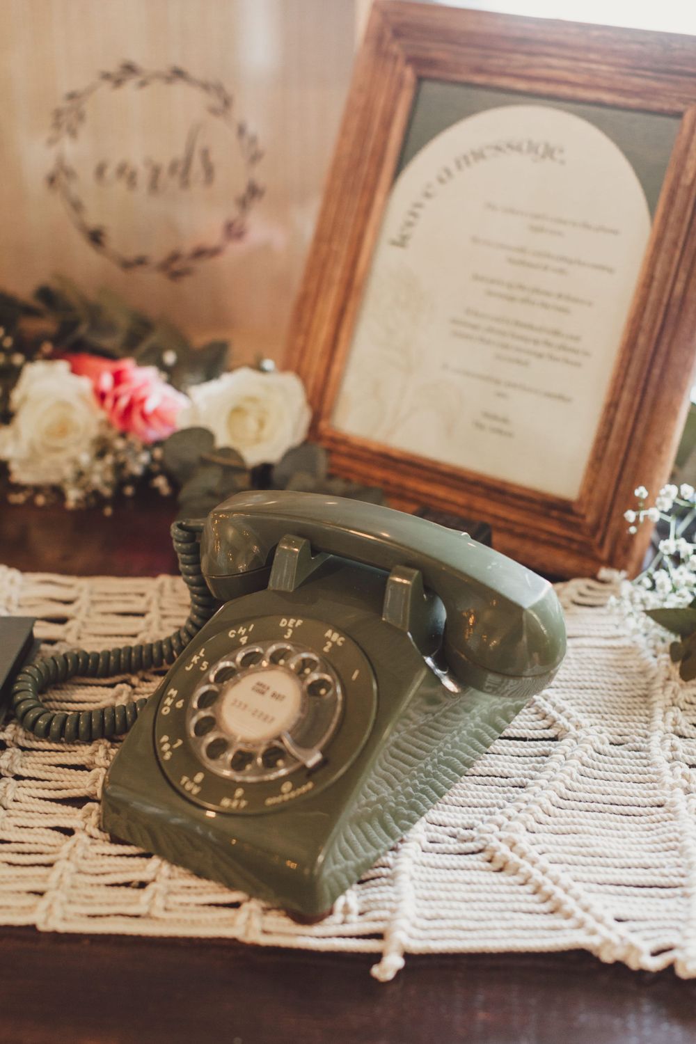 Vintage rotary telephone displayed with framed menu and floral decor on lace tablecloth.