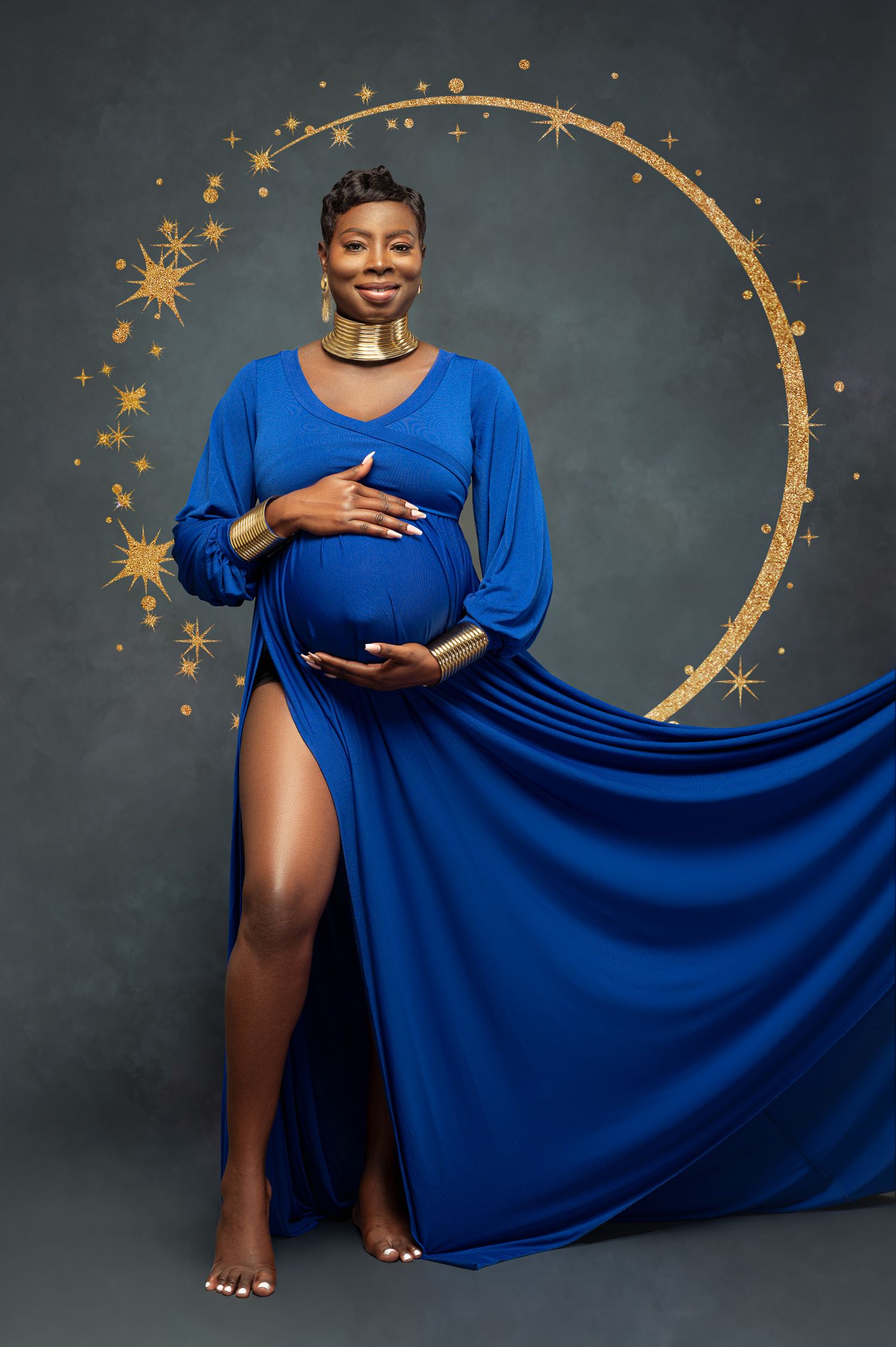 A maternity photoshoot featuring a flowing royal blue dress against a dark backdrop with golden moon and star decorations.