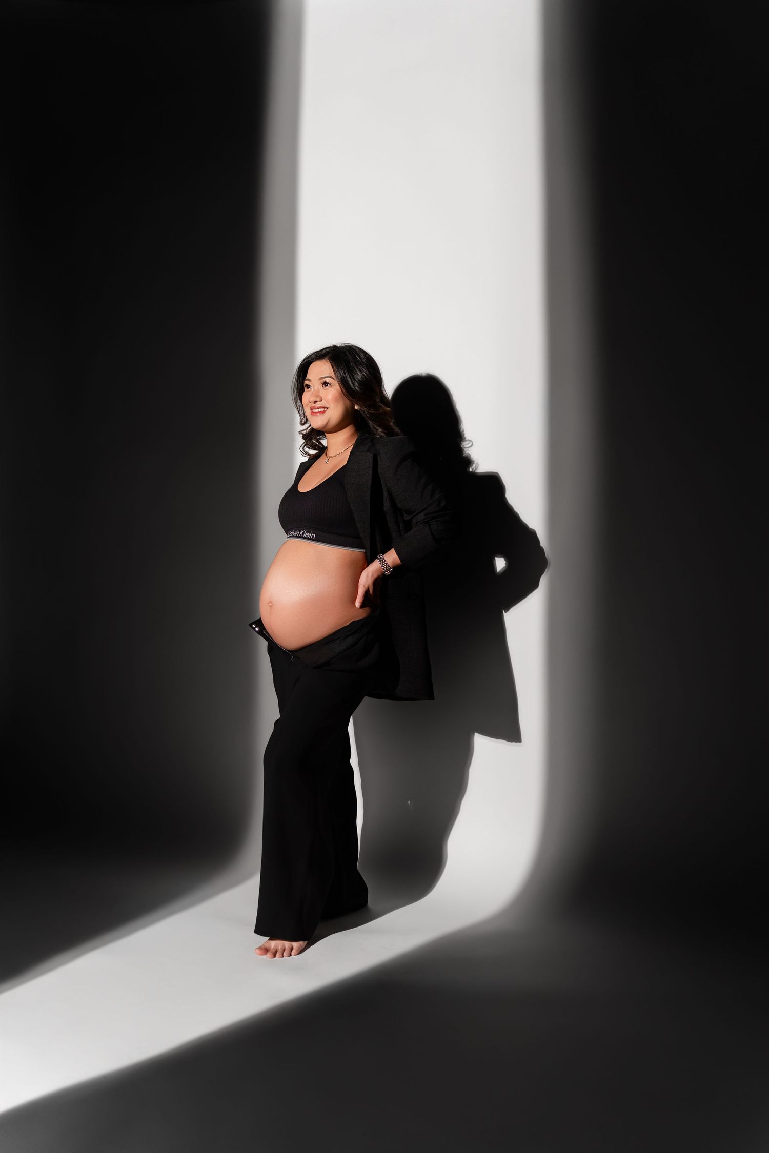 Artistic black and white maternity photo series showing a pregnant woman in shadows against a white backdrop.
