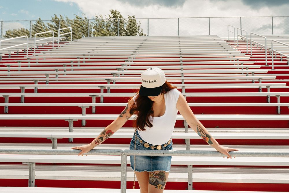 Woman in denim shorts walking across empty red and white stadium bleachers on a sunny day.