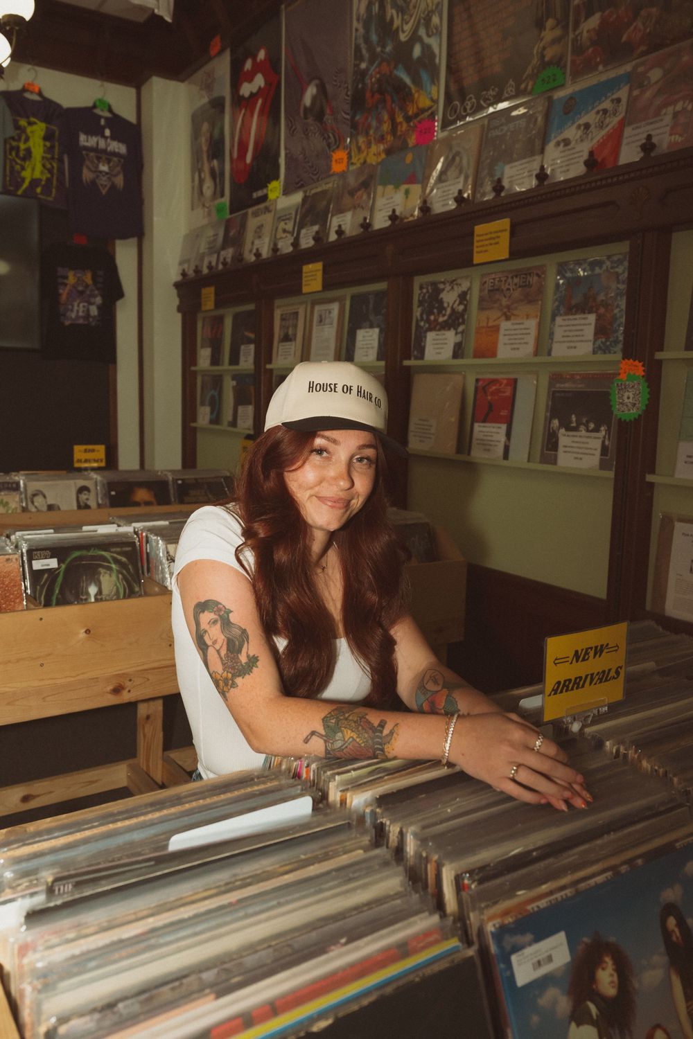 Person browsing through vinyl records in a music store with shelves of albums visible in the background.