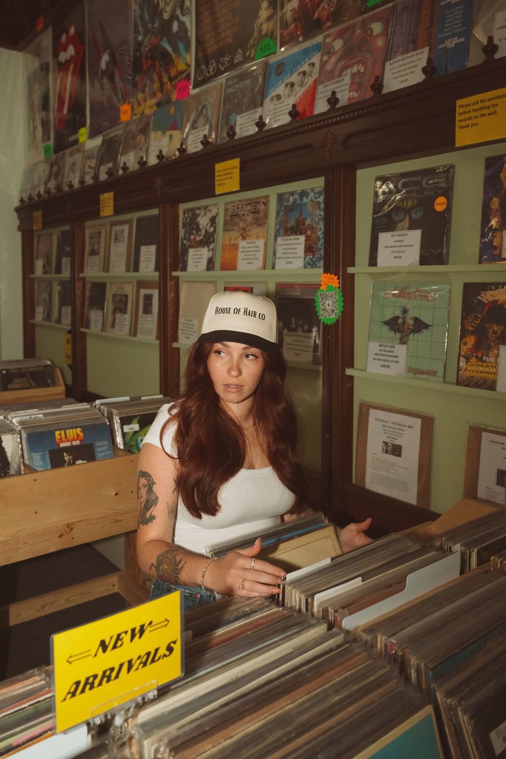 Person browsing through vinyl records in a music store with posters and album covers on the walls.