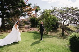 Wedding party poses for photos on a lush green lawn with tropical trees in the background.