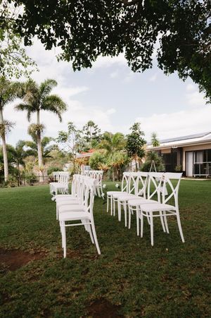 White cross-back chairs arranged in rows on a lawn with palm trees for an outdoor wedding ceremony.