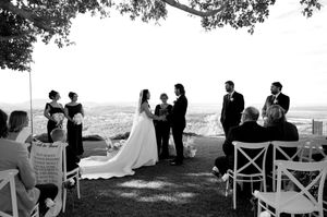 An outdoor wedding ceremony taking place under trees with a scenic mountain backdrop.