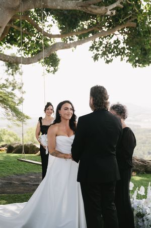 Wedding ceremony guests gather under a large tree during an outdoor celebration with scenic views.