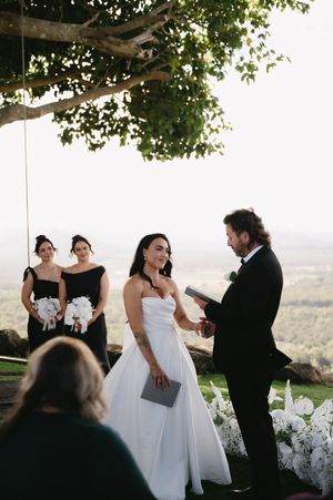 Wedding ceremony taking place outdoors under trees with scenic mountain views.
