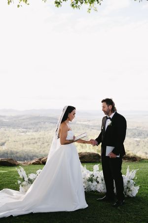 Elegant outdoor wedding ceremony with white chairs and floral decorations against a scenic backdrop.