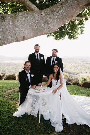 Wedding party gathered under a large tree during outdoor celebration.