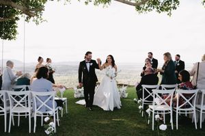 A wedding ceremony processional on a hilltop with white chairs and scenic views.