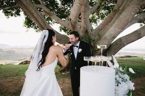 A couple shares a drink together under a large tree during their wedding reception.