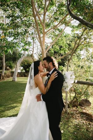 Romantic wedding photos of newlyweds sharing intimate kisses under green trees in a garden setting.