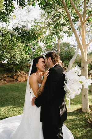 Romantic wedding moment shared under white flowering trees in a garden setting.