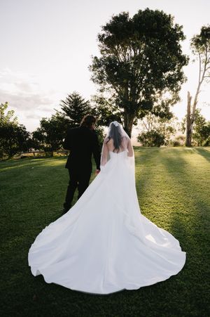 A flowing white wedding dress spreads across green grass during an outdoor sunset photo session.