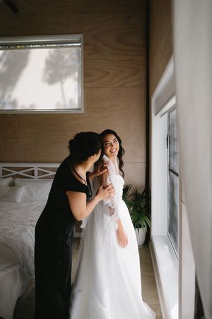 Wedding dress preparation moments captured in warm tones showing dress adjustments in a modern room.
