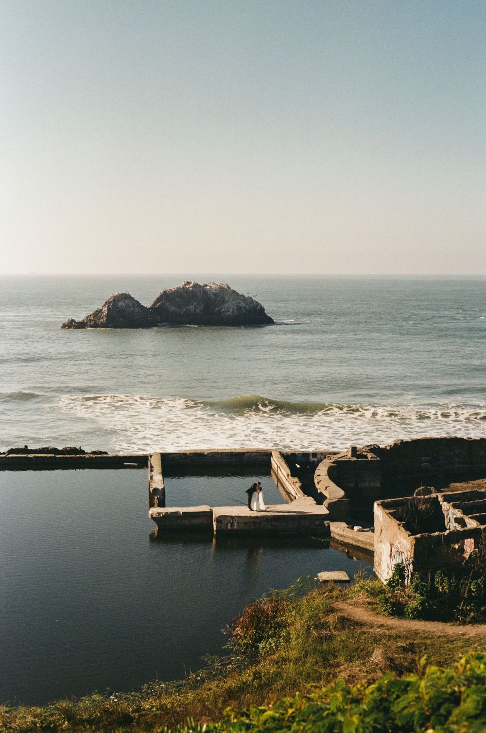 Rocky island formation in the ocean with a stone pier in the foreground.