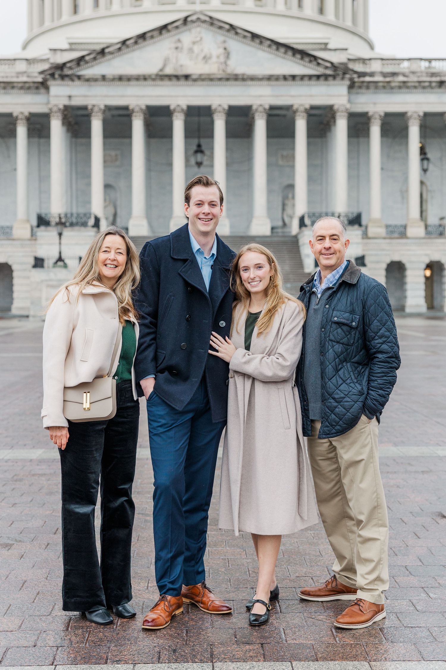 A group poses for photos in front of the US Capitol building on a cloudy day.