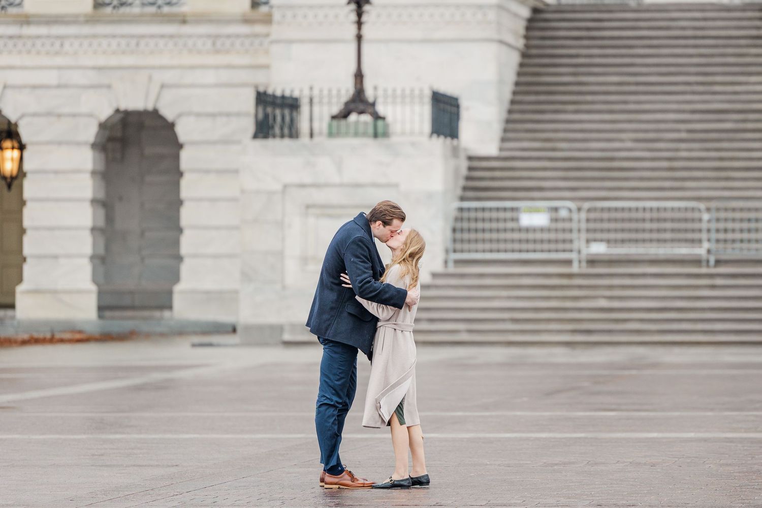 A couple shares a romantic moment embracing on stone steps outside a grand historic building.