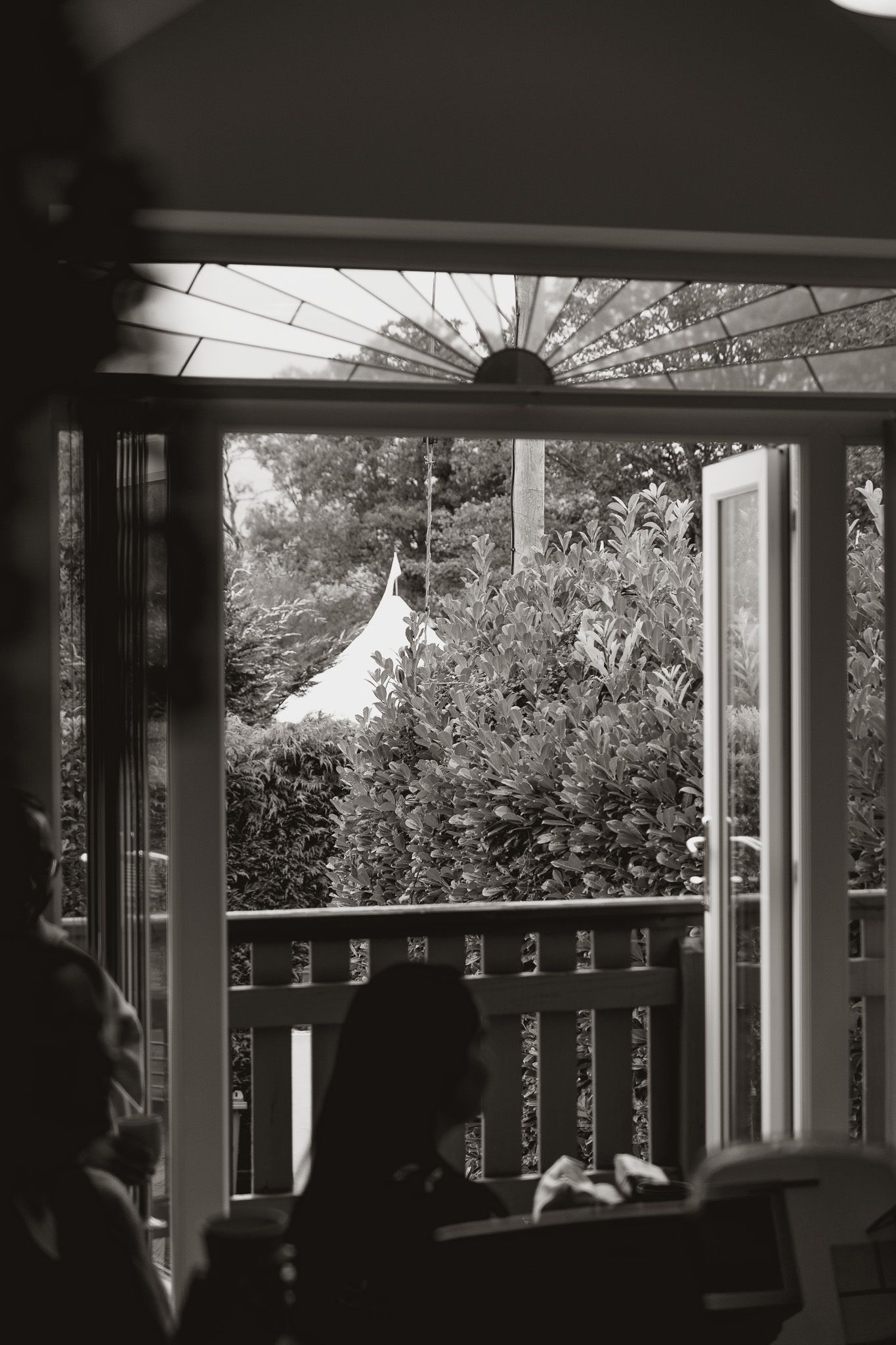 A black and white panoramic view through a porch window shows silhouettes of columns and railings against a bright sky.