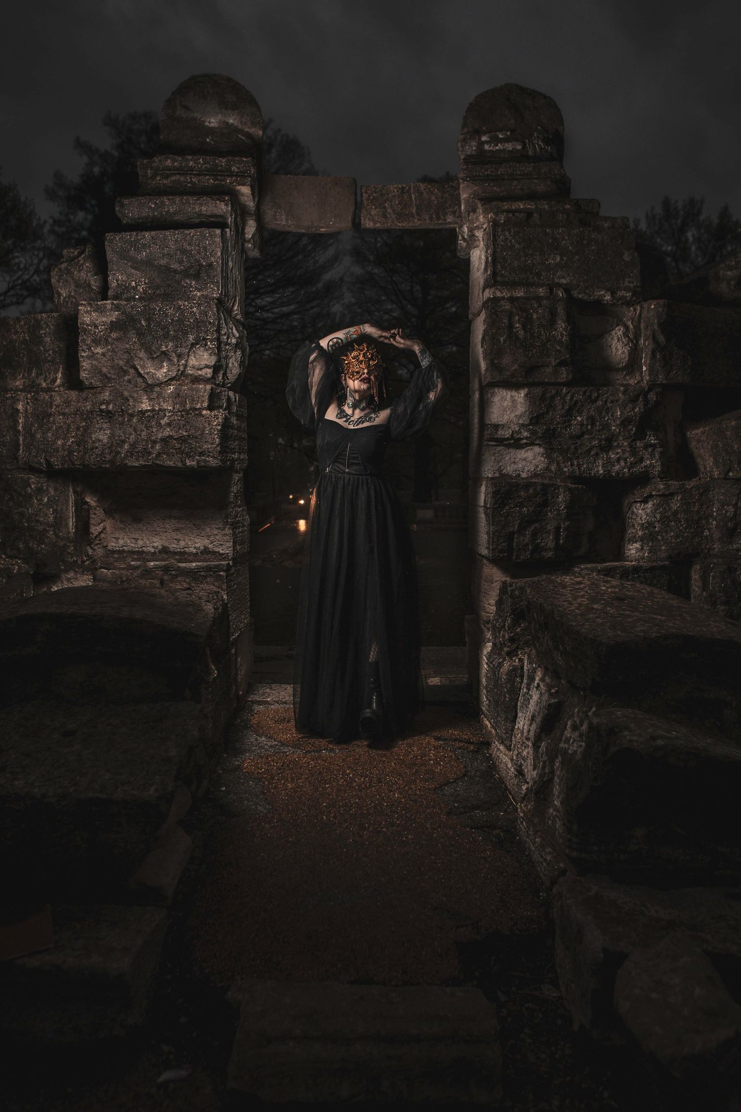 Gothic figure in black dress standing among ancient stone ruins at night.