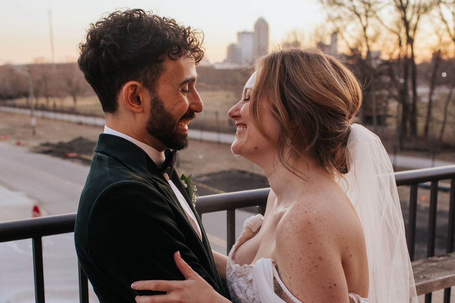 A bride and groom share intimate moments at sunset on a rooftop with the city skyline in the background.