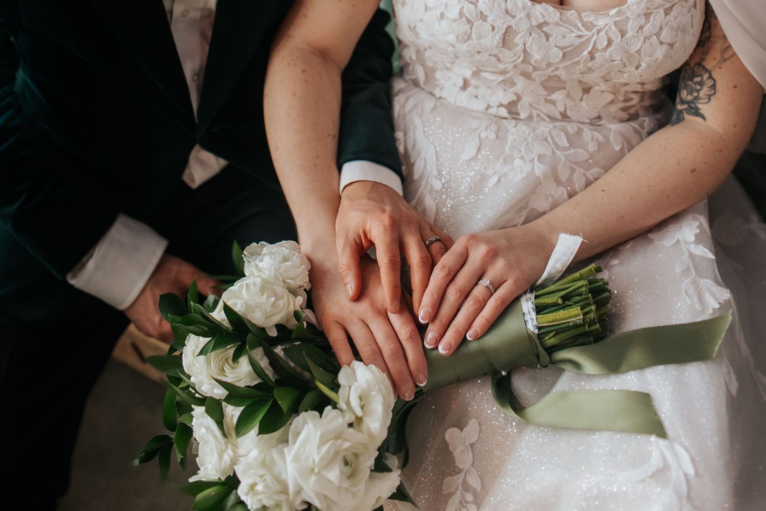 A close-up detail shot of white wedding bouquet and lace dress against a dark background.