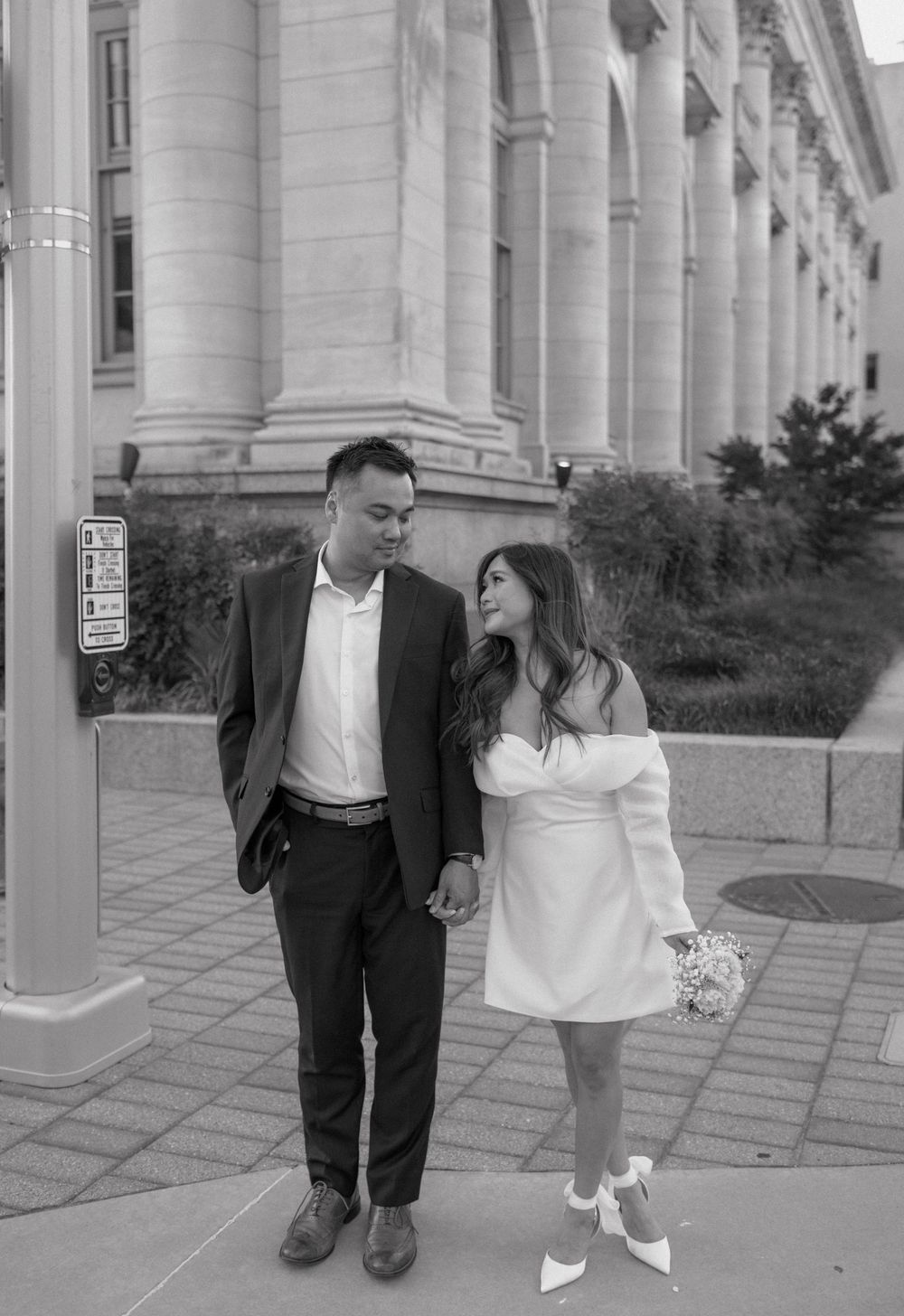 A black and white photo series showing a couple walking together and posing playfully in front of a columned building.