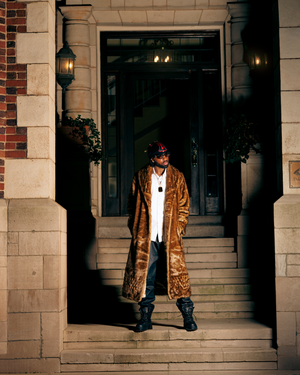 Person wearing brown leather jacket stands in front of stone building facade with brick accents.