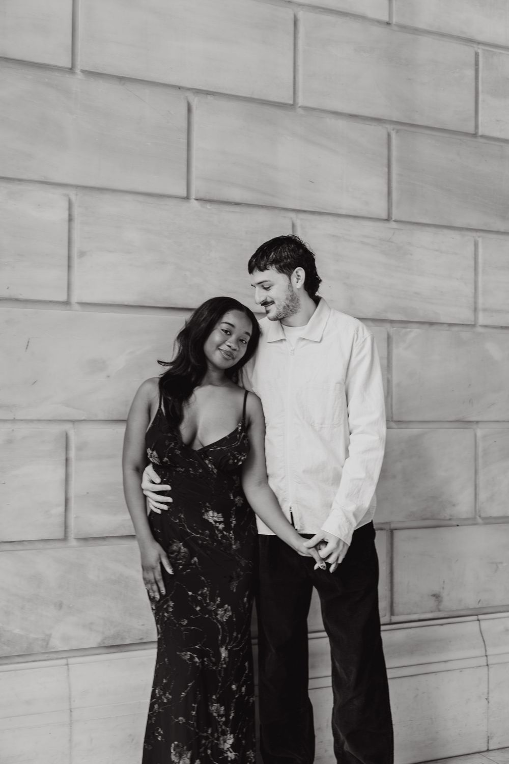 A couple shares a joyful moment together against a light stone wall in a series of candid black and white photos.