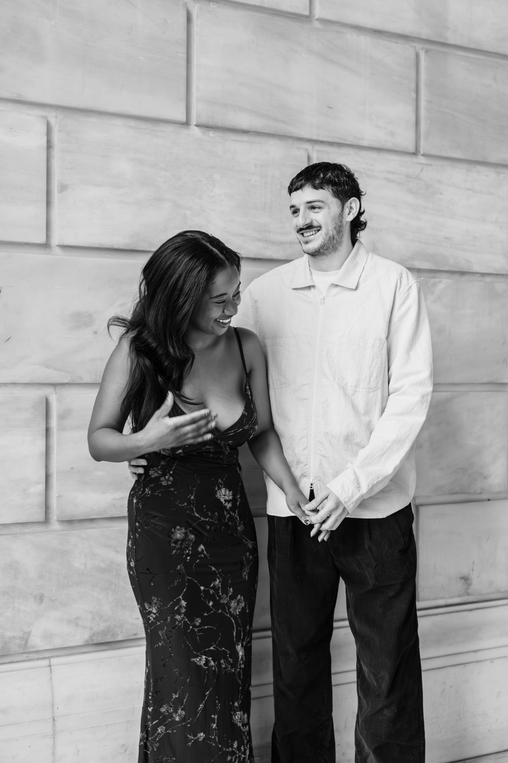 A couple shares a playful moment in black and white against a stone wall, shown in three progressive frames.