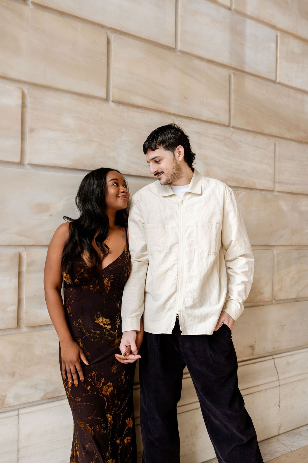 A couple shares a tender moment together while standing against a beige stone wall.