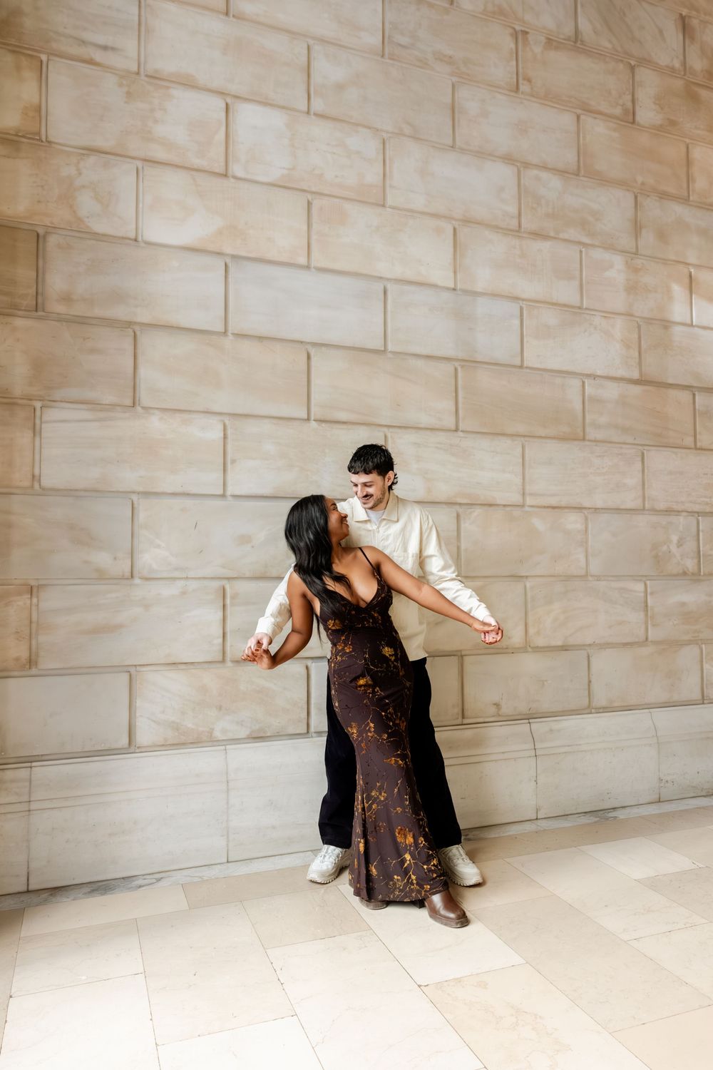A sequence showing a person in a dress sliding down against a beige stone wall in an artistic performance.