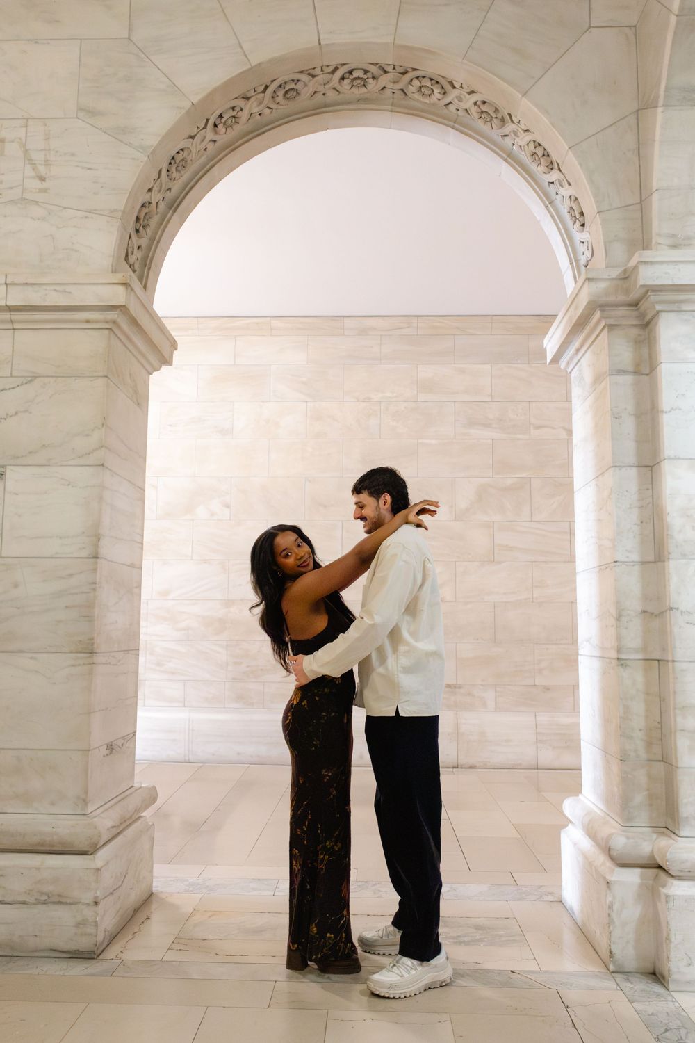 Two dancers perform an elegant duet beneath ornate marble arches in a classical architectural setting.