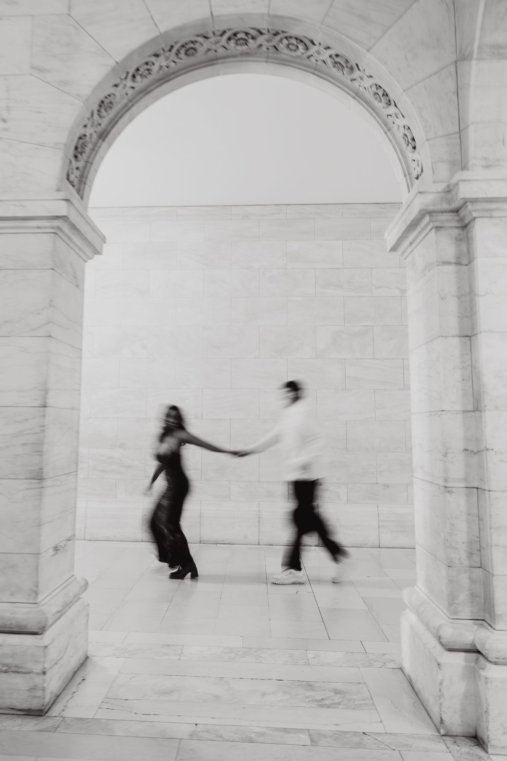 Motion-blurred figures dance through a bright marble colonnade creating a dramatic artistic effect.