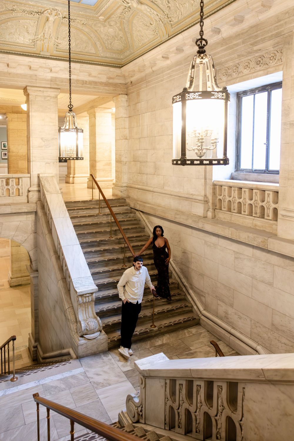 Elegant marble staircase with ornate details and hanging lanterns in a historic building interior.