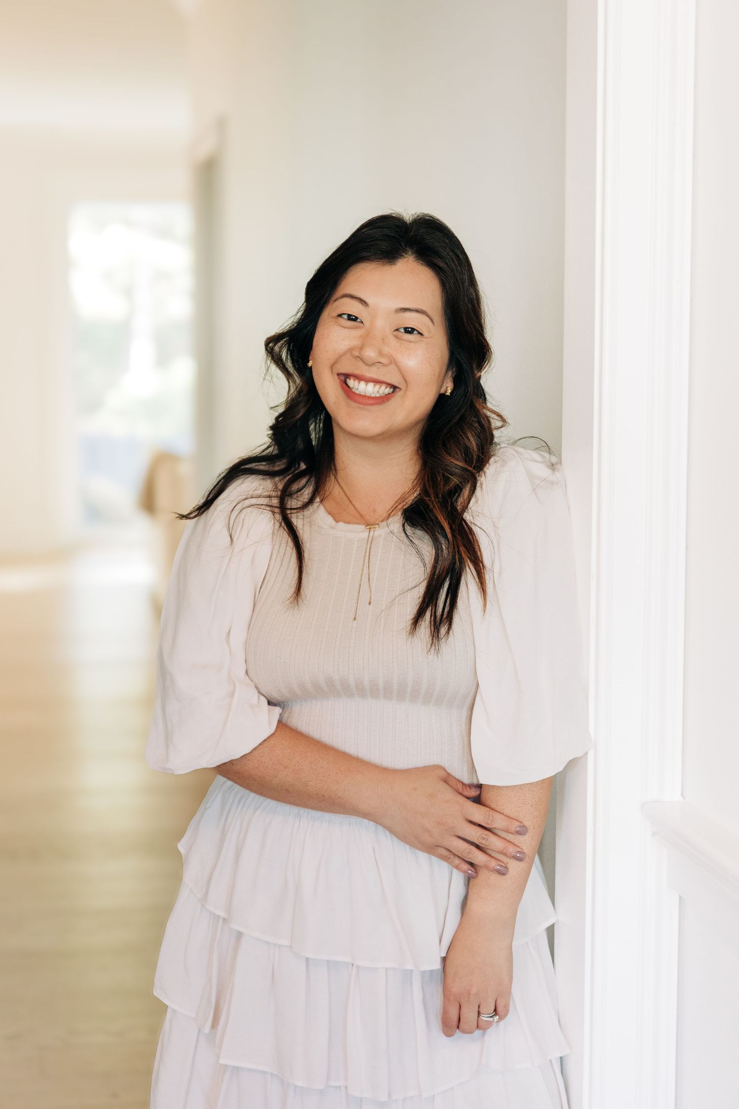 A person wearing a white ruffled dress poses joyfully against a bright interior wall in a lifestyle photoshoot.