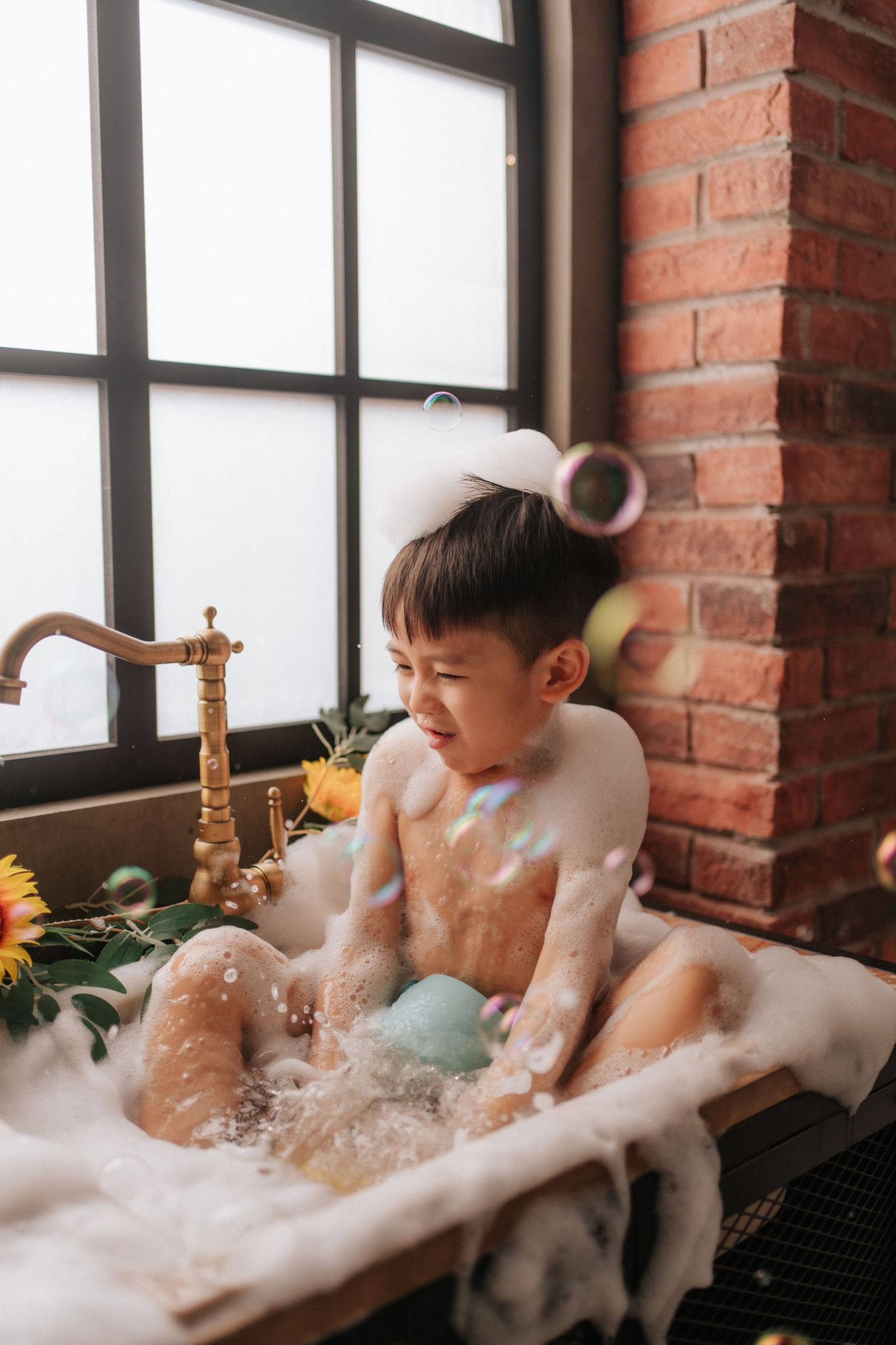 Baby in floral dress sits with yellow sunflowers and white decorations during a professional photo session.