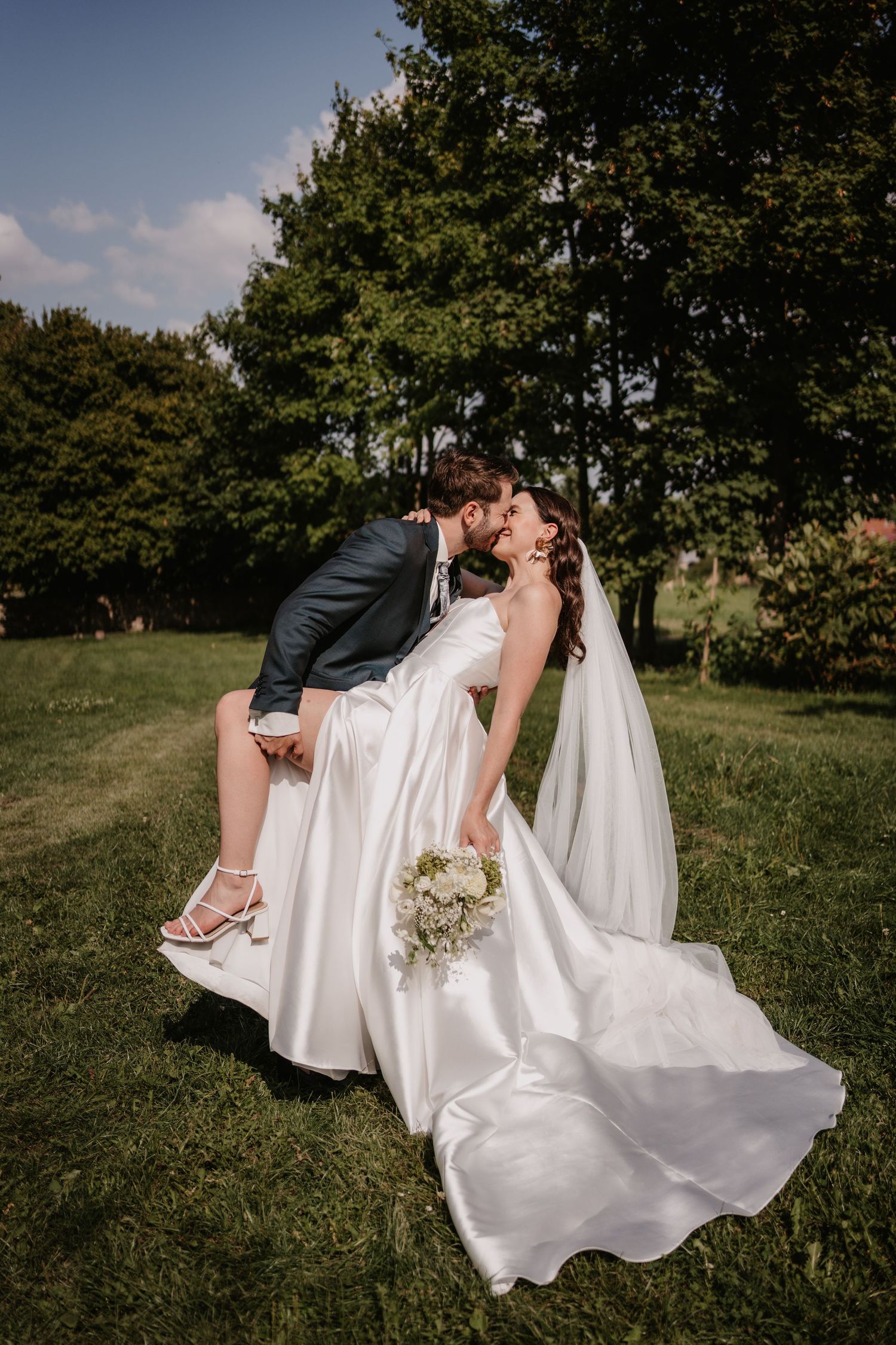 A romantic wedding couple in a grassy field shares an intimate dip pose in their formal attire.