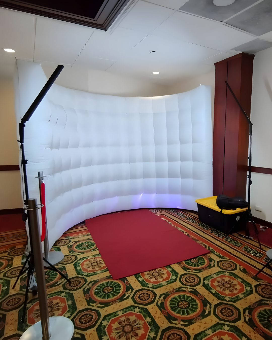 An inflatable white curved wall structure is installed in a room with ornate carpeting and dark wood trim.