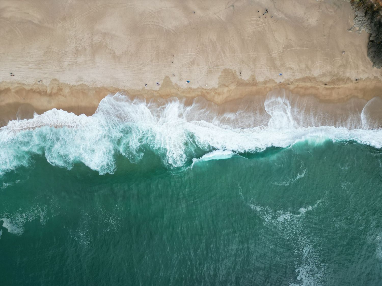 Aerial view of turquoise ocean waves crashing against a white sandy beach creating a dramatic coastline pattern.