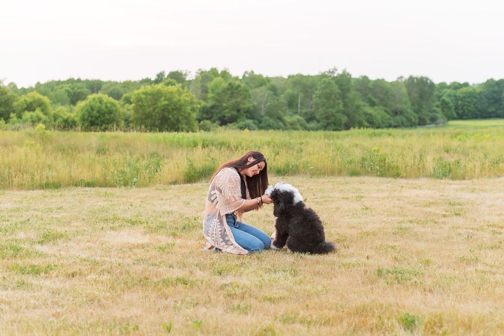A person lies in a grassy field with a dog on a sunny summer day.
