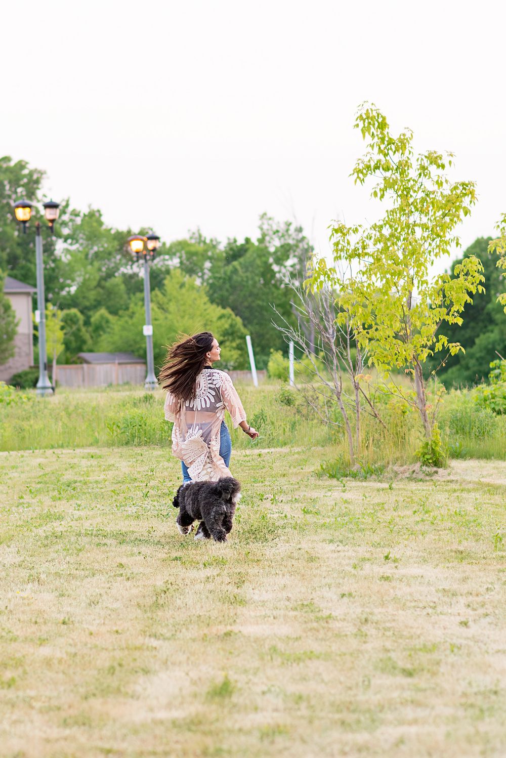 A person in casual attire crouches down in a grassy field on a sunny day while taking photographs.