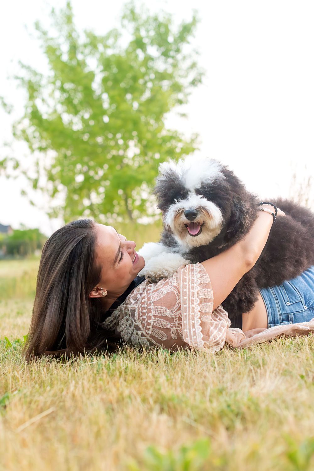 Person and small dog share a tender moment while relaxing together in tall grass on a sunny afternoon.