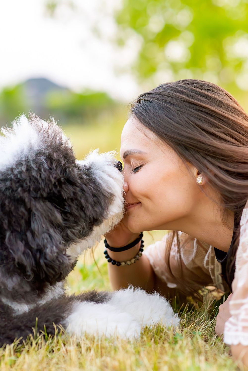 A person lying in grass gives affectionate kisses to a small black and white dog in a series of photos.
