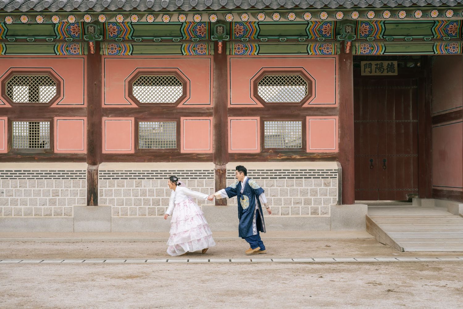 Traditional Korean palace courtyard with ornate wooden architecture and stone pathways under overcast skies.